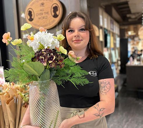 Forskellige kunstige blomster i vase som medarbejder holder 